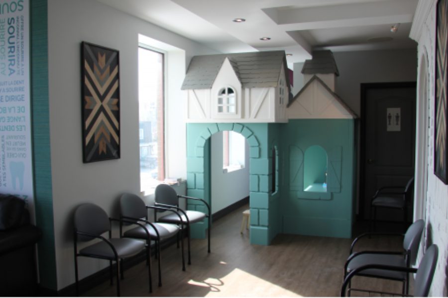 Le coin des enfants dans la salle d’attente : une maisonnette de jeu bleu-vert, près de la fenêtre et des chaises.