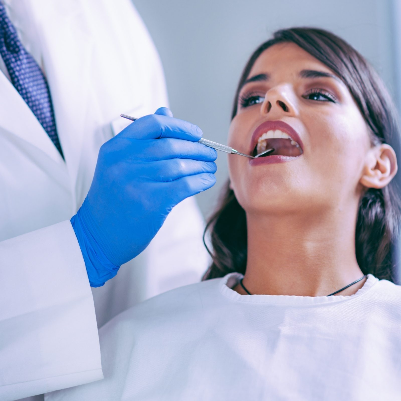 Une personne installée dans le fauteuil pendant que le dentiste examine ses dents au miroir.