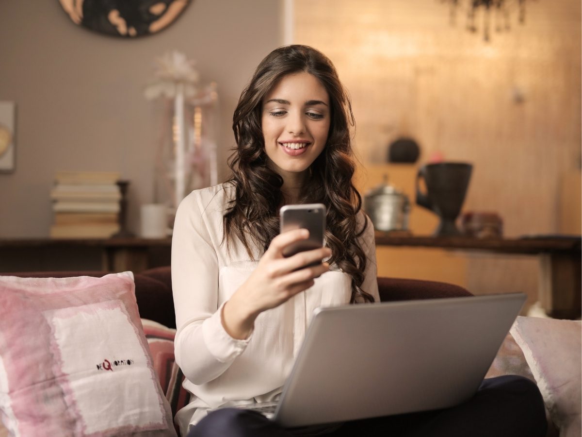 Une personne assise avec un ordinateur portable et un téléphone à la main.